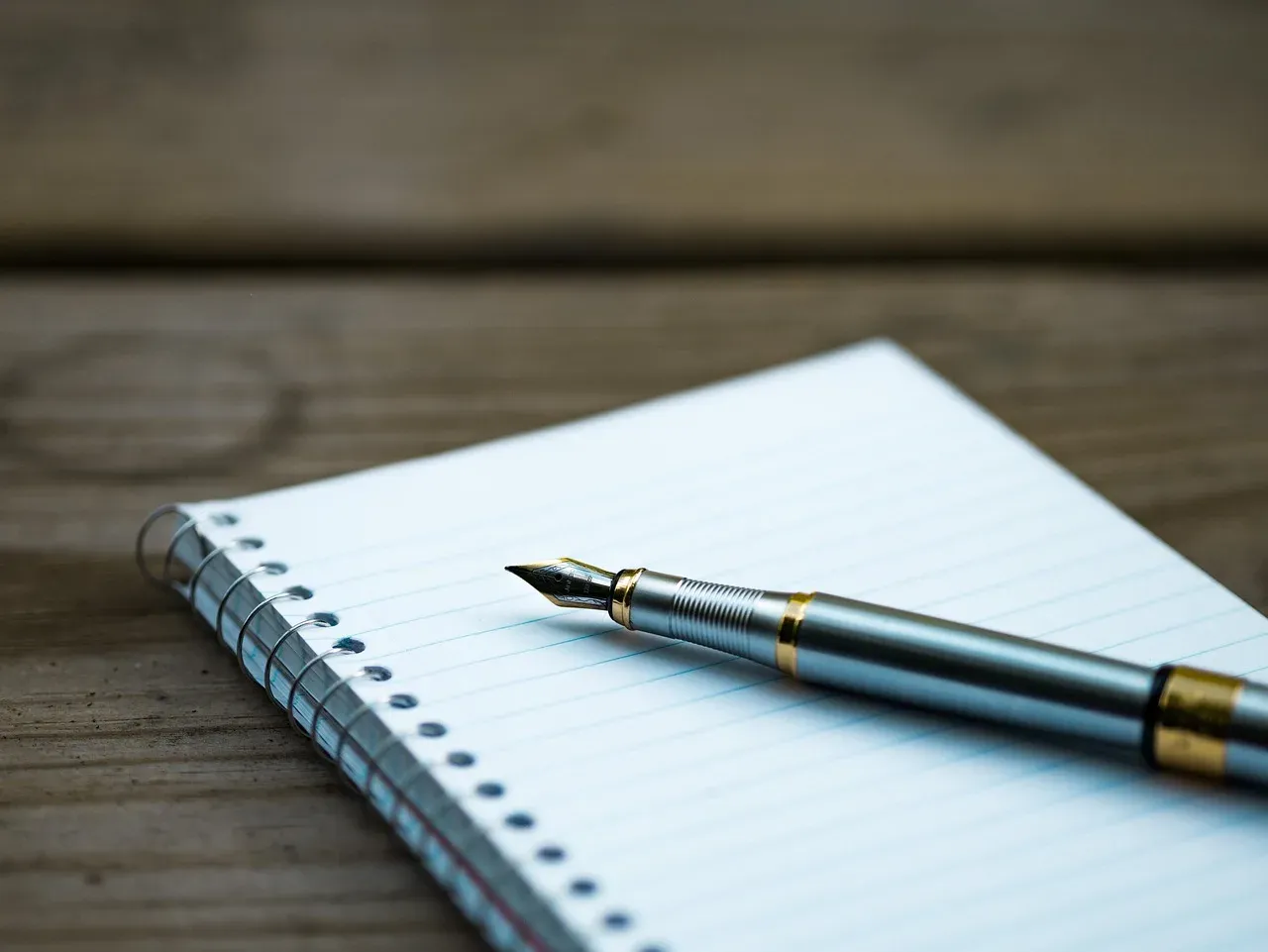 Un cahier à spirale fermé avec un stylo plume posé dessus, sur une table en bois.