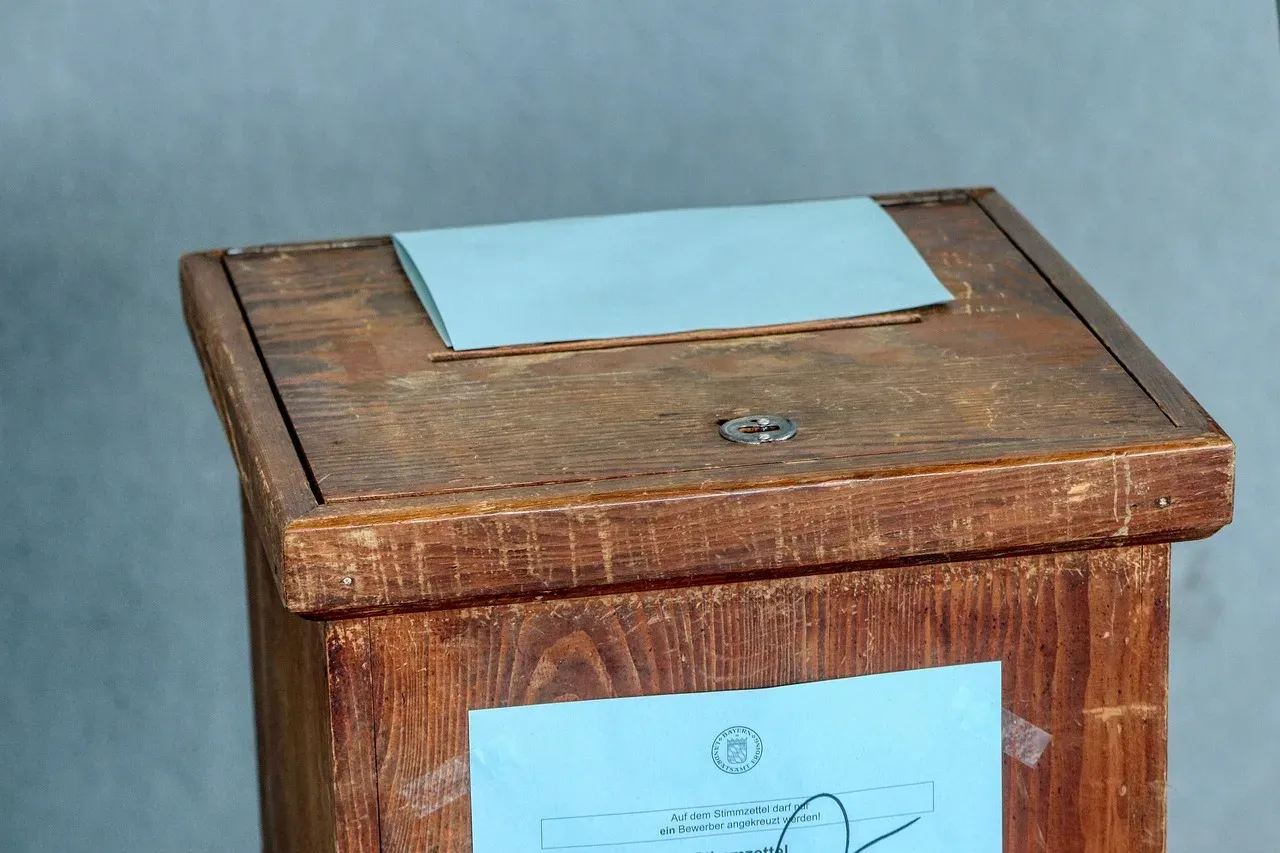 Une urne électorale en bois ancienne, sur laquelle sont posés un bulletin de vote bleu et un formulaire.