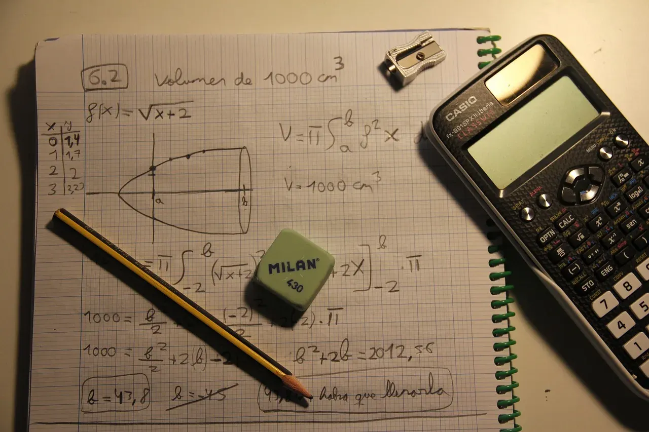 Un cahier ouvert couvert de formules mathématiques manuscrites, avec une calculatrice, un crayon et une gomme posés dessus.